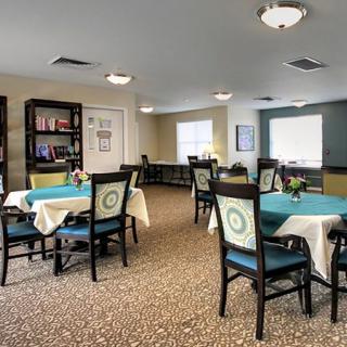 A well-lit dining area with tables and chairs, featuring bookshelves along the wall.