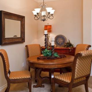 A cozy dining room with a round wooden table and upholstered chairs, decorated with a mirror, chandelier, and various decorative items.