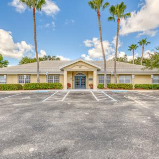 A single-story building with palm trees and a parking lot under a partly cloudy sky.