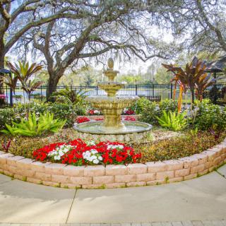 A beautifully landscaped garden with a central fountain, surrounded by vibrant flowers and lush trees.