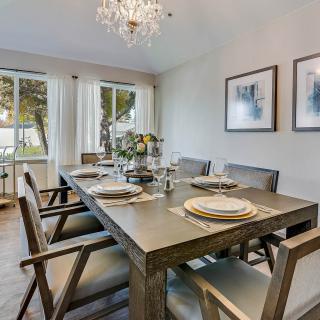 A modern dining room with a wooden table set for a meal, illuminated by a chandelier and featuring minimalist decor and artwork.