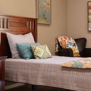 A cozy bedroom with a neatly made bed, decorative pillows, and a comfortable chair adorned with a colorful throw.