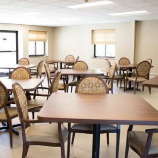 An empty dining area with multiple tables and chairs, well-lit by natural light from the windows.