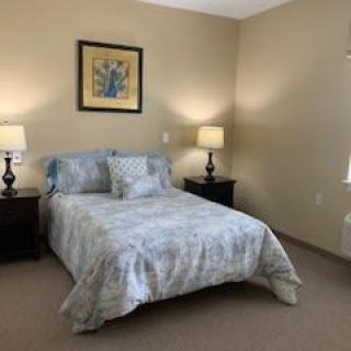 A neatly arranged bedroom featuring a bed with patterned bedding, two bedside lamps, and wall artwork.