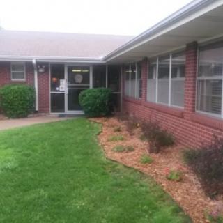 A brick building with a well-maintained lawn and shrubbery leading to an entrance.