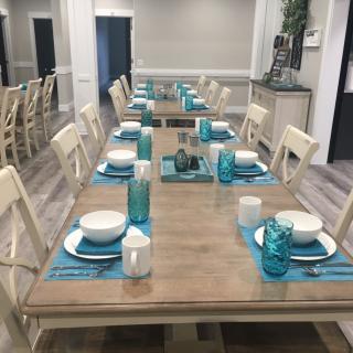 A neatly arranged dining room with a long wooden table, white chairs, and blue accented place settings.