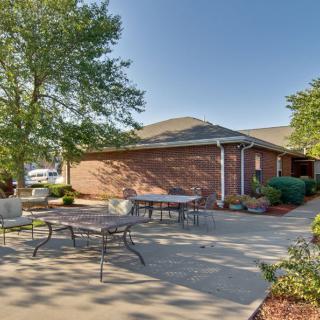A sunny outdoor patio with tables and chairs next to a brick building.
