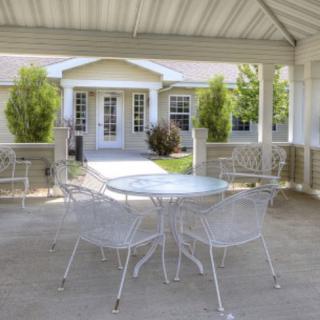 A sunny patio with outdoor furniture under a gazebo, overlooking a garden and house.