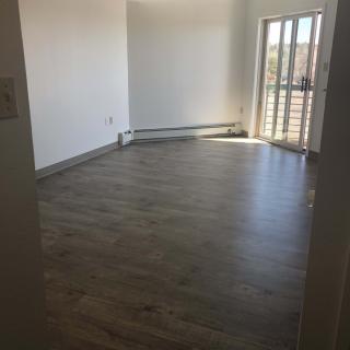 A bright, empty room with hardwood floors and large windows allowing natural light.