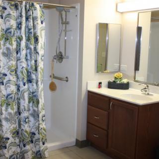 A well-lit bathroom featuring a shower with a floral curtain, a sink with cabinets, and a mirror.