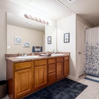 A well-lit bathroom featuring a double sink vanity with wooden cabinets, a large mirror, and a patterned shower curtain.
