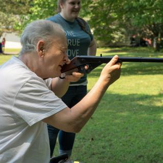 An elderly person aiming a rifle outdoors during a recreational activity.