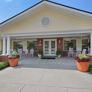 Front view of a building entrance with a porch, columns, and large planters.