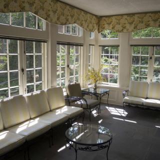 A bright sunroom filled with natural light, featuring comfortable seating and glass tables.