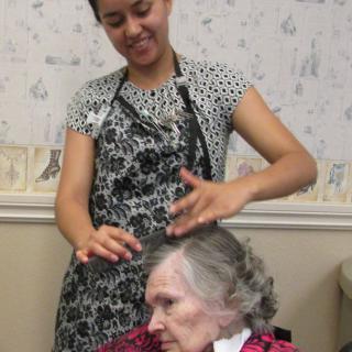 A caregiver styling the hair of an elderly woman in a salon setting.