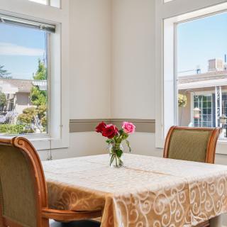 A bright dining room with a table set for four, decorated with a vase of red and pink flowers.
