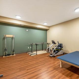 A small exercise room with wooden flooring featuring gym equipment including an elliptical machine, exercise bars, and a workout bench.