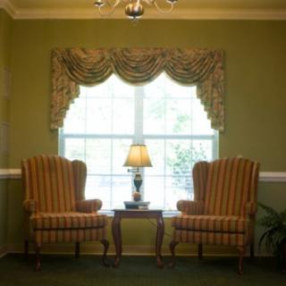 A cozy living room setup with two armchairs, a lamp on a table, and elegant draped curtains framing a window.