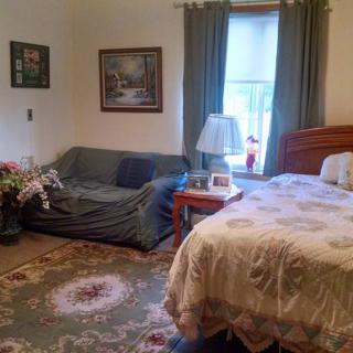 A cozy bedroom with a bed, sofa, and decorative elements such as paintings and a patterned rug.