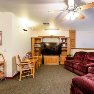 A cozy living room with a large television, comfortable seating, and wooden shelves.