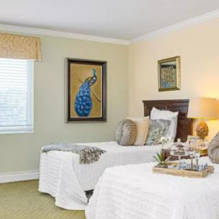 A cozy bedroom featuring twin beds with white linens, a peacock painting, and soft lighting.