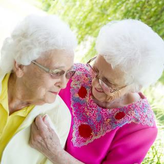 Two elderly women sharing a warm moment outdoors.