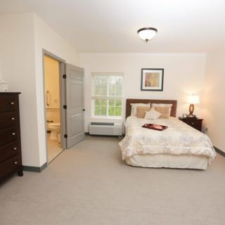 A cozy bedroom with a bed, dresser, and a lamp by the window.
