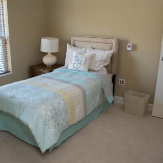 A cozy and calming bedroom featuring a single bed with decorative pillows, a lamp on a nightstand, and light-colored walls.