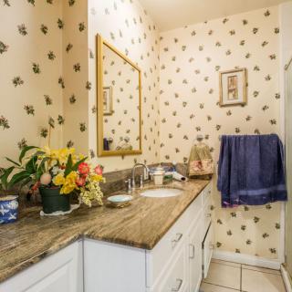 A quaint bathroom with floral wallpaper, a countertop sink, and decorative flowers.
