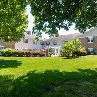 A residential building surrounded by a lush green lawn and trees under bright sunlight.