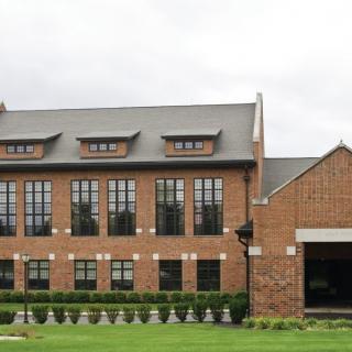 A large brick building with numerous windows set against a landscaped lawn.