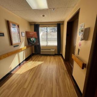 A well-lit hospital hallway featuring wooden flooring and large windows.