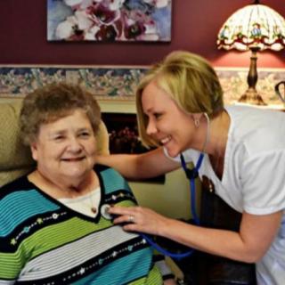 A nurse smiling while examining an elderly patient with a stethoscope.