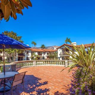 A sunny courtyard with outdoor seating, umbrellas, and surrounding buildings under a clear blue sky.