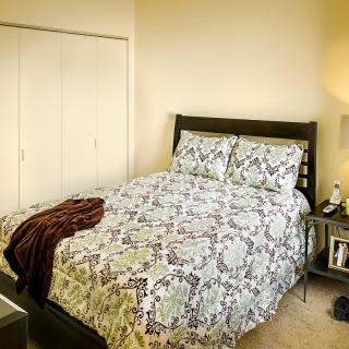 A cozy bedroom with a neatly made bed, patterned bedding, and soft lighting.