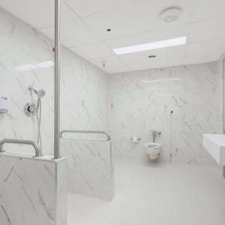 Modern accessible bathroom with white marble walls and safety features.