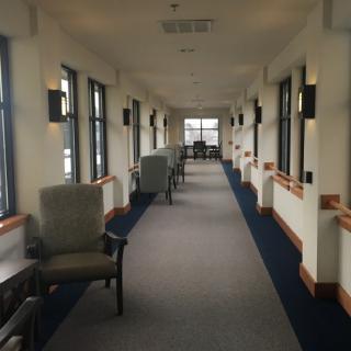 A long, well-lit hallway with chairs and windows lining the sides.