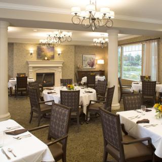 Elegant dining room with neatly arranged tables and chairs, featuring chandeliers and a fireplace.