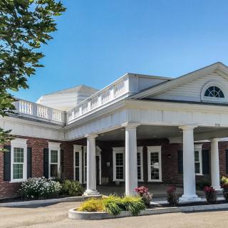 A colonial-style building with white columns and landscaped entrance under a clear blue sky.