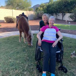 Two women outdoors with a horse grazing nearby.