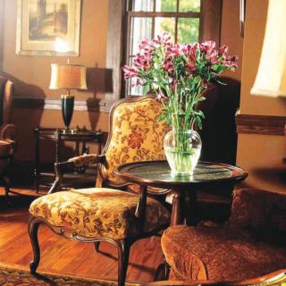 A cozy living room featuring vintage furniture with a floral arrangement on a side table, creating a warm and inviting atmosphere.