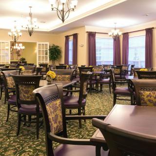 A spacious dining room with elegant furnishings and chandeliers, featuring numerous tables and chairs arranged neatly.