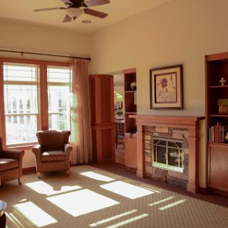 A cozy living room with warm wood tones and soft sunlight streaming through the large windows.