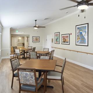 A spacious dining room with wooden tables and chairs, adorned with framed art on the walls and illuminated by ceiling fans.
