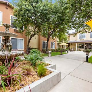 A landscaped apartment courtyard with a central fountain and surrounding trees.