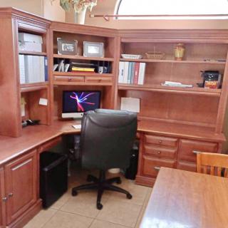 A tidy home office setup with a corner desk, computer, and bookshelves.