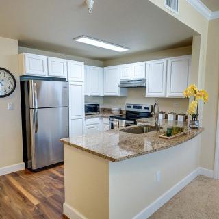A modern kitchen with stainless steel appliances and granite countertops, featuring white cabinets and a hardwood floor.