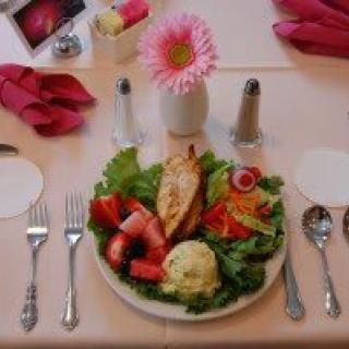 A beautifully set dining table featuring a plate of salad with chicken, garnished with vegetables and accompanied by elegant table decor including a pink flower in a vase.