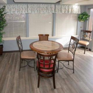 A cozy dining area with a round table and four chairs, featuring large windows and indoor plants.