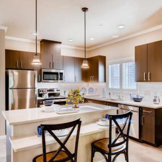 A modern kitchen with stainless steel appliances and a central island, featuring pendant lighting and bar stools.